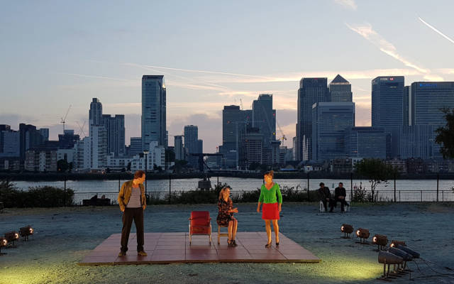 A-View-from-the-Bridge-de-Roovers, GDIF 2017. Three actors perform on an outdoor stage in Greenwich with Canary Wharf behind.