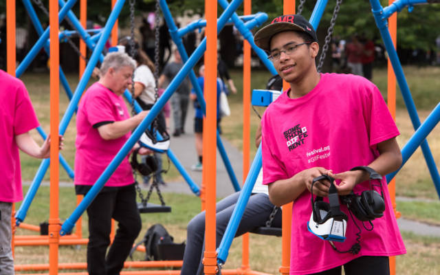 A volunteer in a pink t-shirt hands out VR headsets at Greenwich Fair, at GDIF.