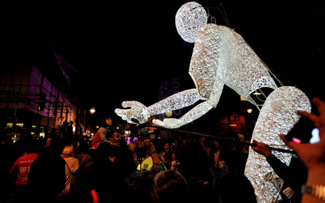 Sense of Unity, DUNDU, GDIF 2017. A giant light-up puppet reaches towards a crowd at a nighttime performance.