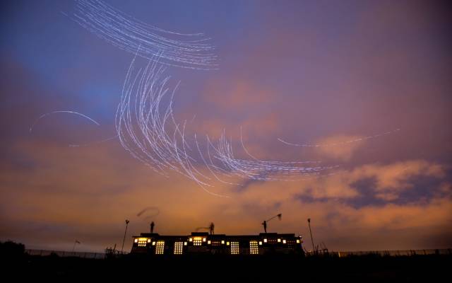 Fly by Night, Duke Riley, LIFT, GDIF 2018. Lights swirl above a building in a sunset sky in Thamesmead, created by pigeons.