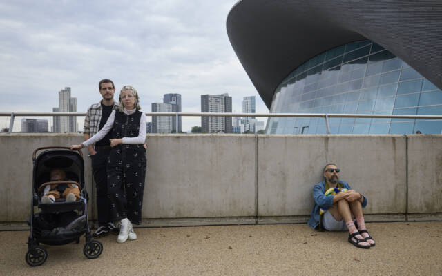 A family of three on the left side of the frame. Behind them is a city scene featuring a modern city glass building